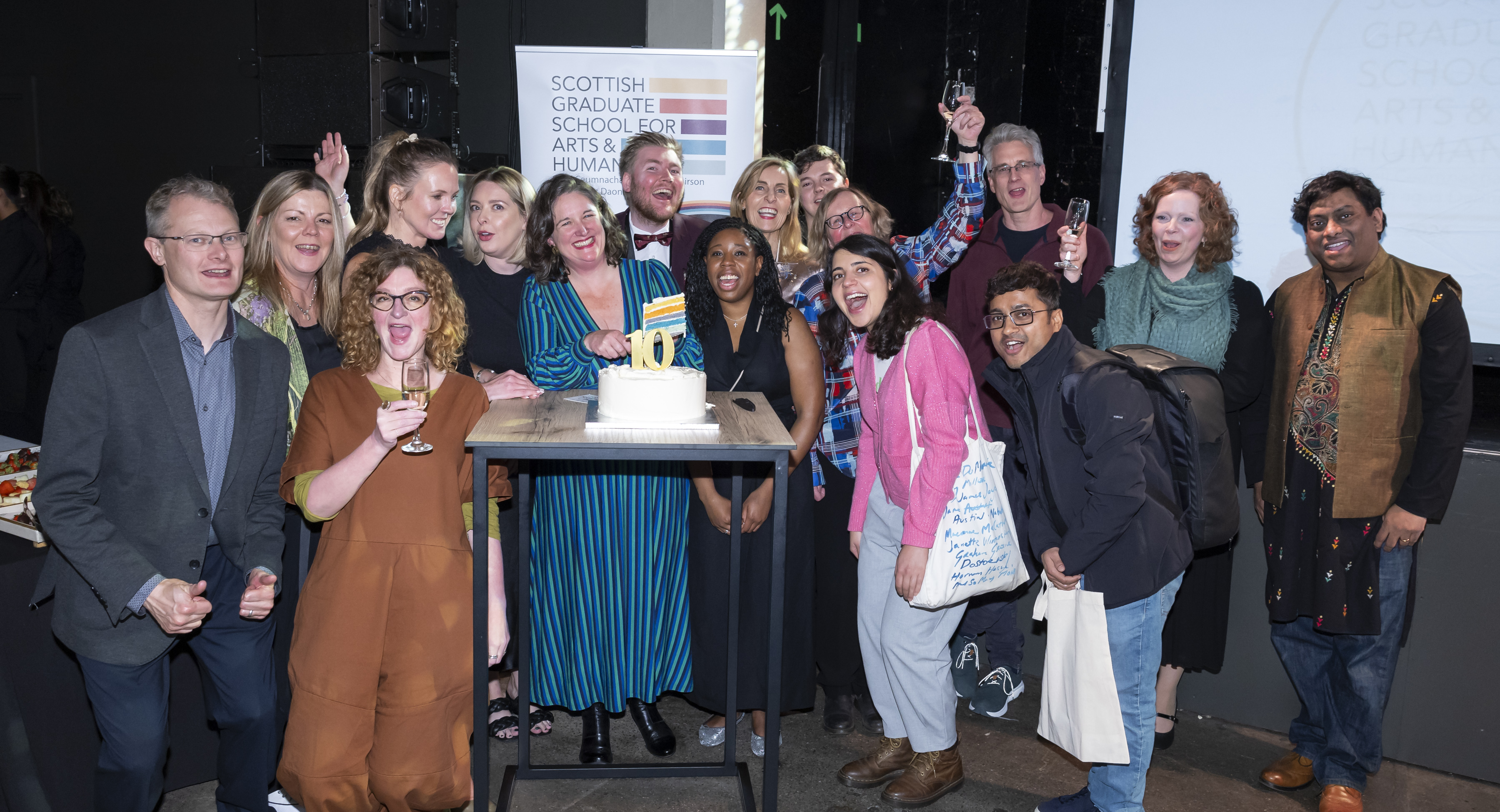 a group posing by a rainbow cake