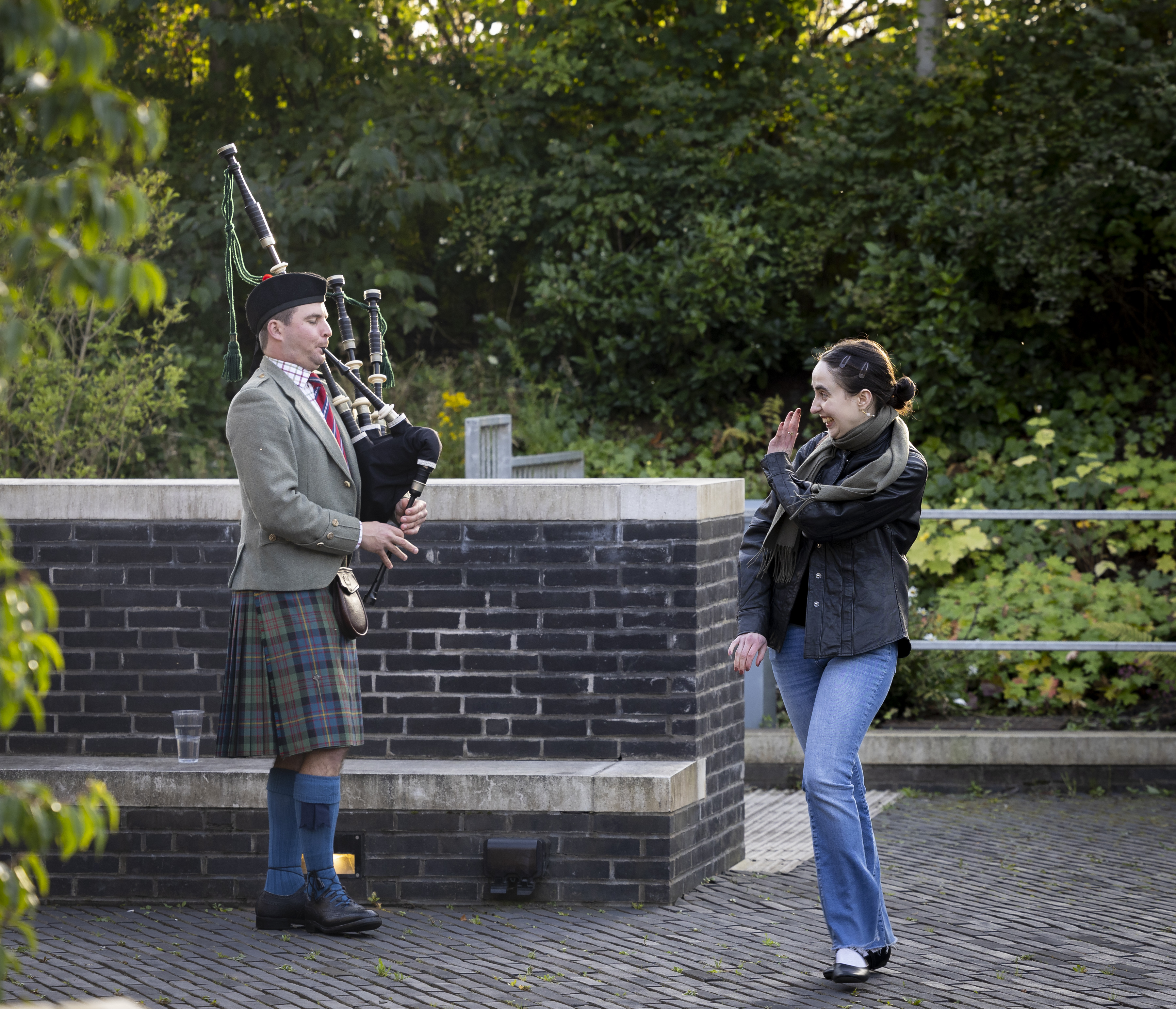 A person waving at a piper with trees in the background