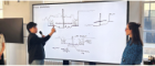 Two people stand in front of a large screen displaying hand-drawn architectural sketches