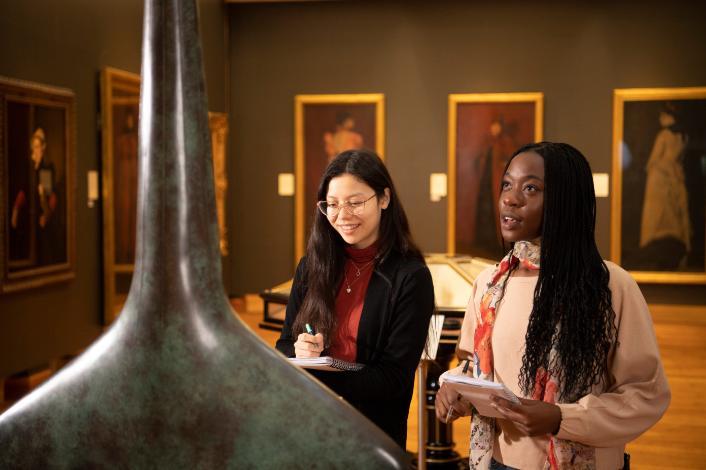 Two students in an art gallery inspecting a sculpture