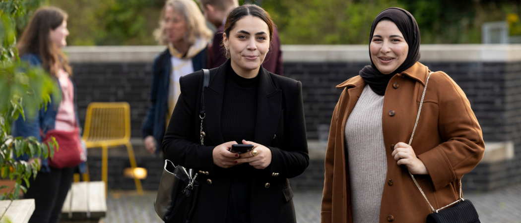 two women smiling outdoors on a campus walkway