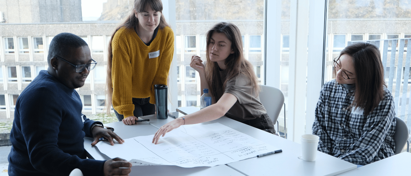 Four people gathered around a table, discussing notes and papers during a workshop or group activity
